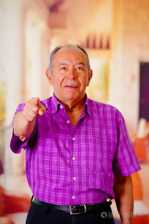 快乐的老人指着他的手在前面和模糊的背景中穿紫色方形t恤的特写