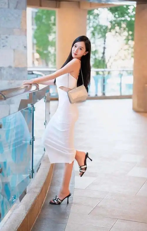 她身穿一件修身的白色连衣裙,配上高跟鞋和修长的双腿,展现出优雅和