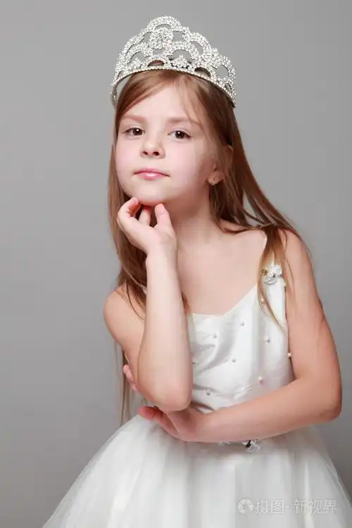 的笑容摆在灰色的背景上的摄像头白色连衣裙的美丽头发的白种人小女孩