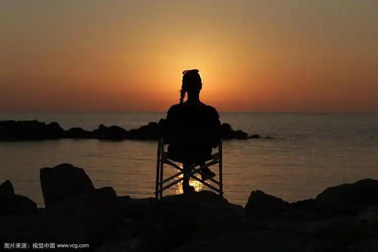 日落时坐在海边椅子上的女人的剪影