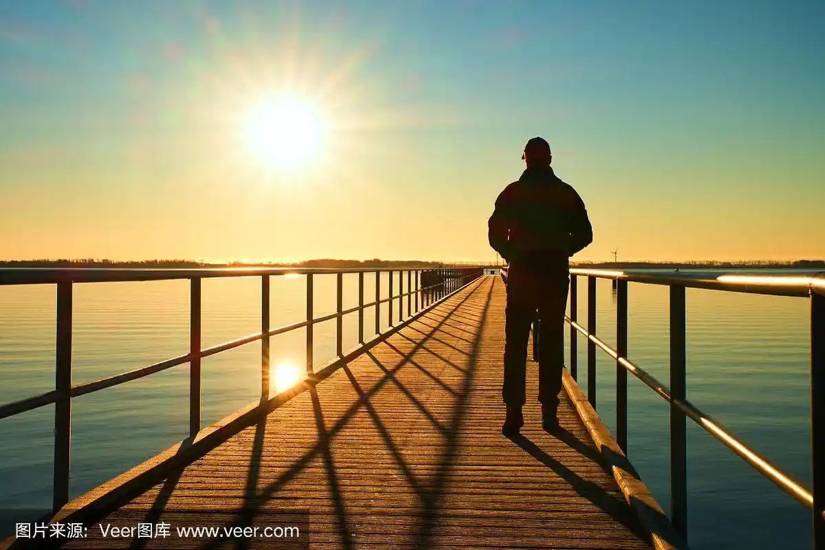 男子剪影走在码头上向太阳走去.美妙的早晨.