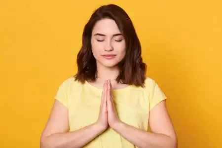 女性双手合十水平拍摄的年轻女子穿着休闲服,在摄影棚的黄色背景上