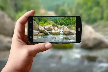 个手持智能手机在屏幕上拍摄自然.在社交网络上发布的山河照片.