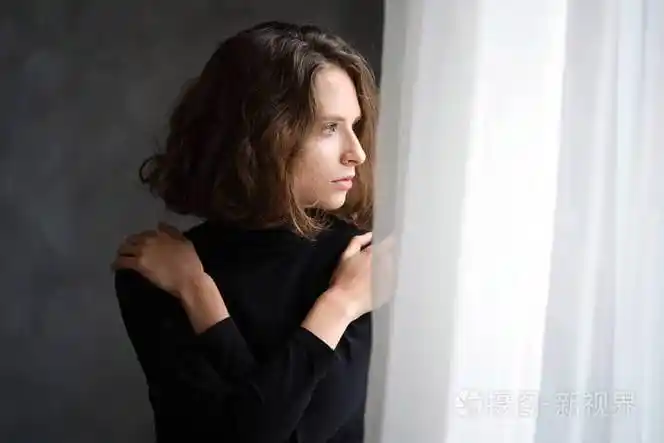 美丽的女孩抱住自己的肩膀若有所思地看着窗外