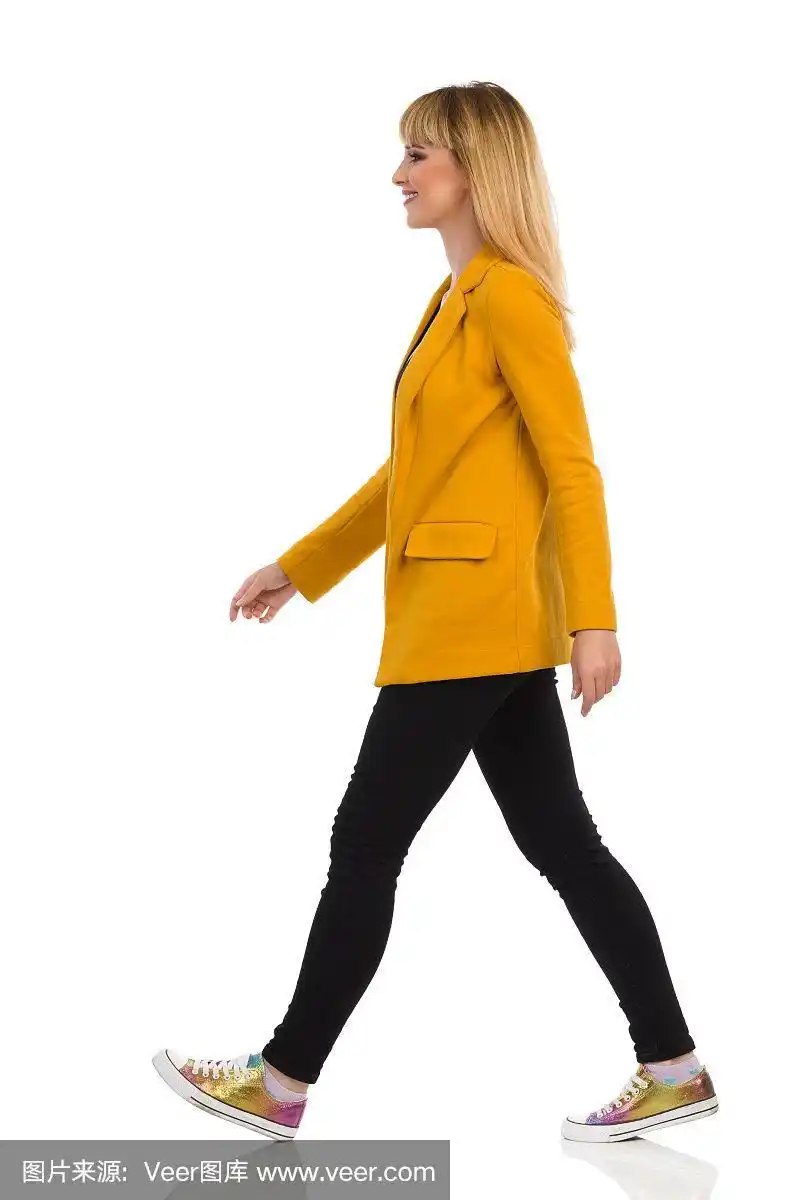 穿着黄色夹克和运动鞋的年轻女子正在走路.侧视图.