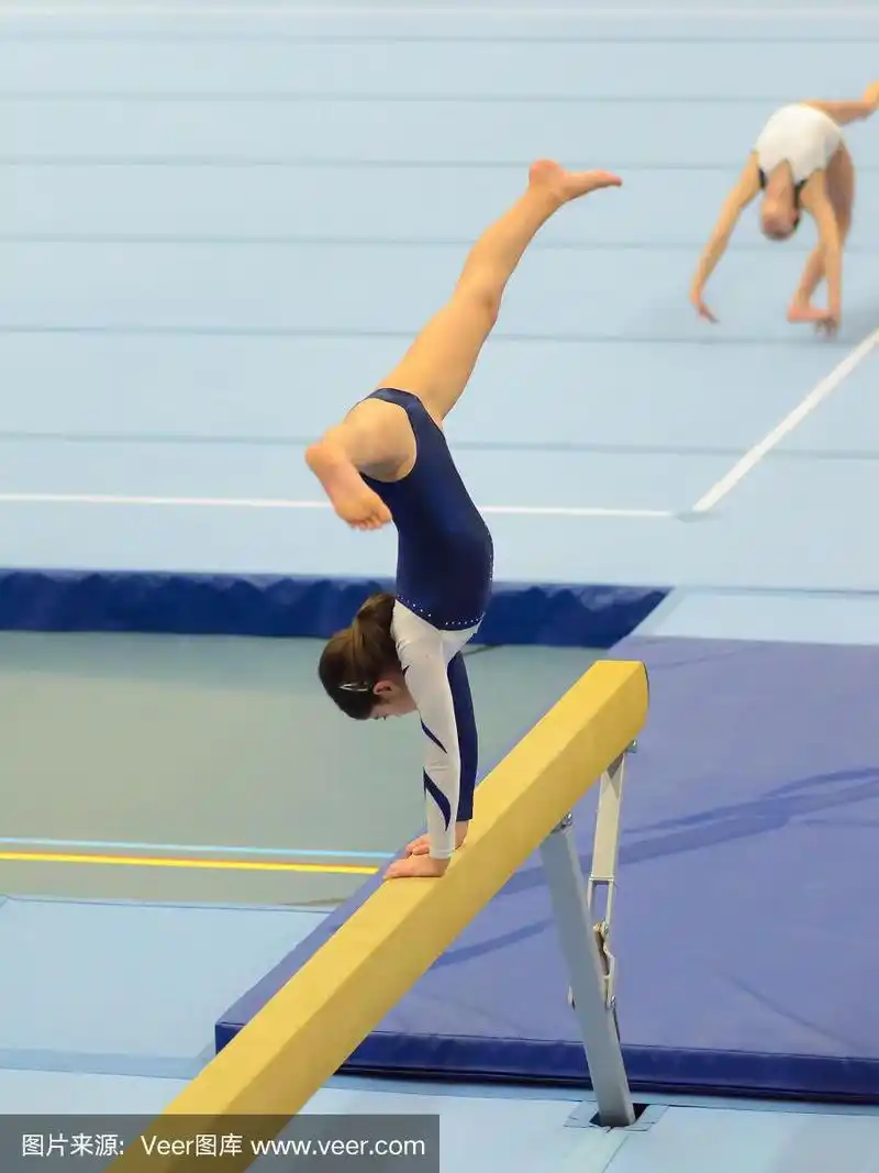 年轻的体操女孩在平衡木上表演常规动作