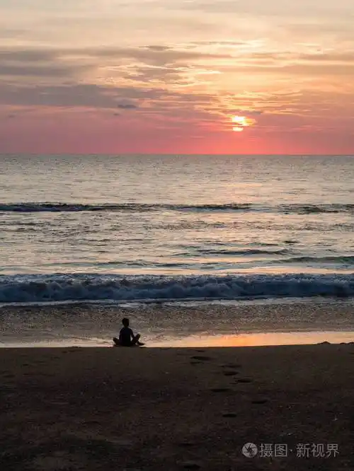 美丽的夕阳下一个不确定的人在沙滩上荷花姿势的剪影日落时冥想一个