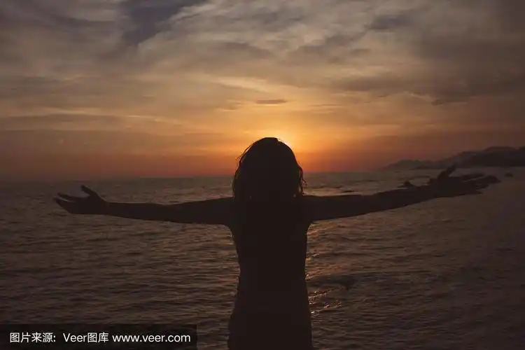 坚强自信的女人在海边的日出下张开双臂