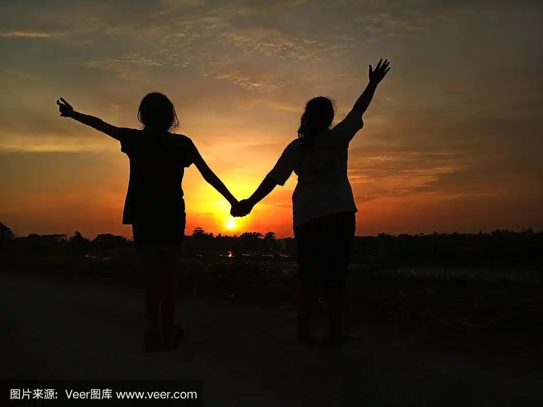 两个年轻的女孩牵手在夕阳的剪影背景.