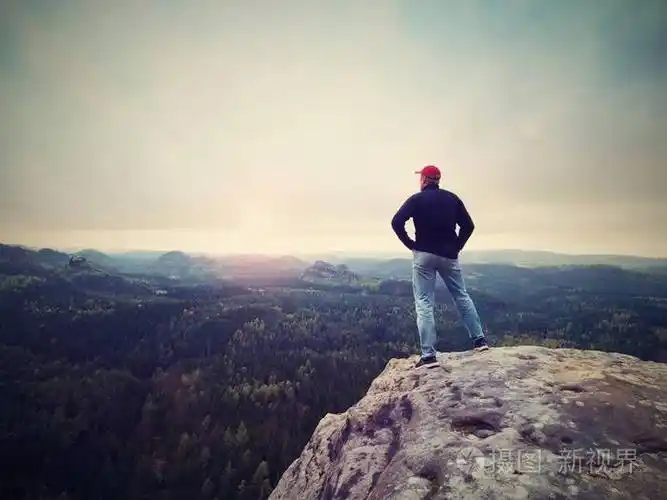 徒步旅行者爬上了山顶欣赏景色.男人看在早晨谷