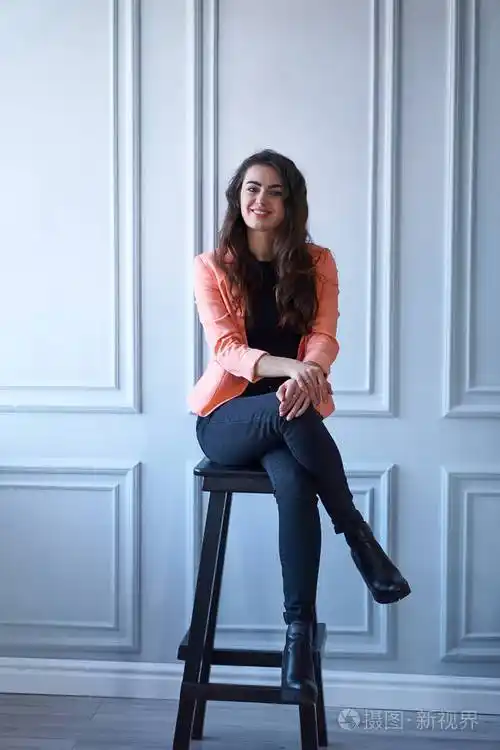 一个穿着桃红色夹克坐在椅子上的迷人的黑发女孩的肖像