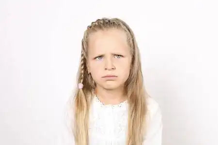 四岁的小女孩与金发, 辫子, 身着白色衬衫, 皱着眉头不满意的面部表情