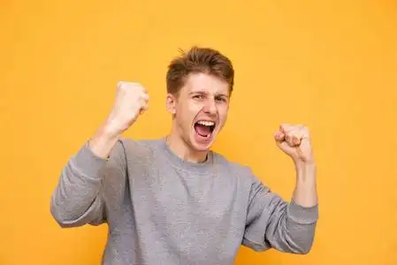 情绪激动的年轻人穿着休闲服装,情绪愉悦的胜利看着黄色背景上的相机.