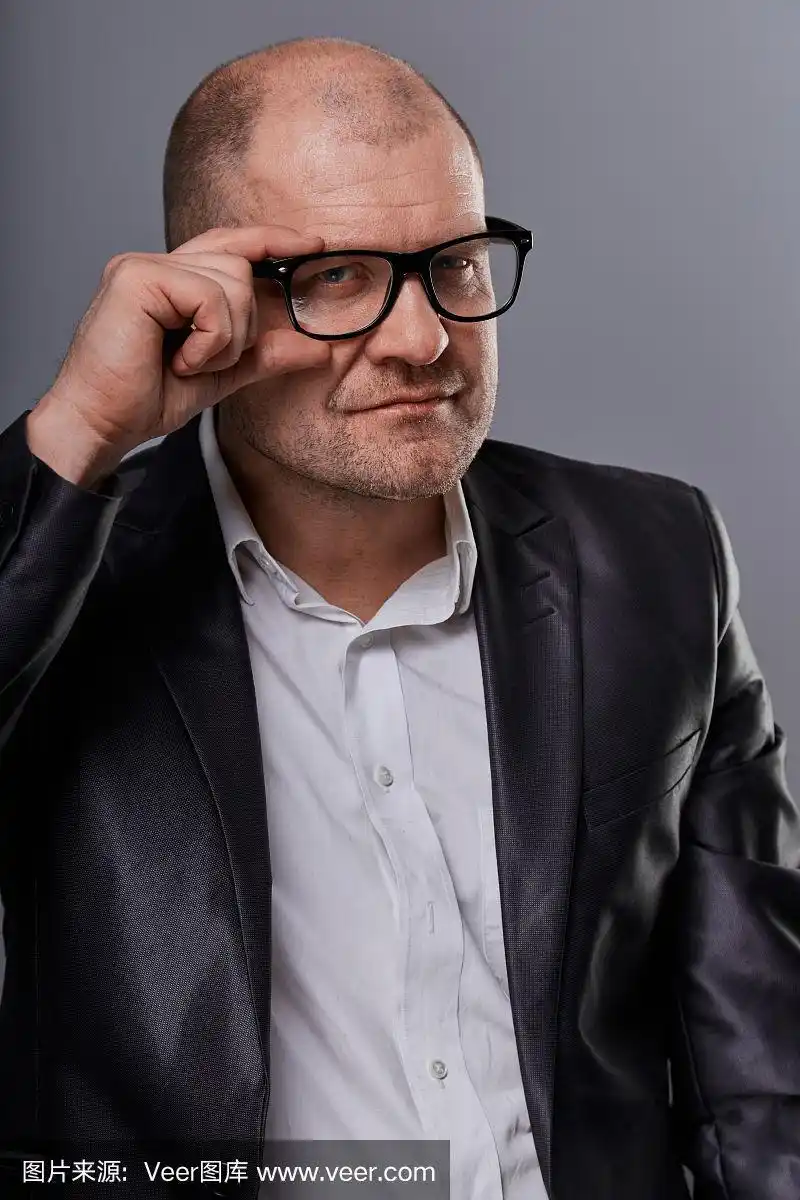 在灰色背景下,一个戴着眼镜的光头商人看起来很严肃.特写镜头