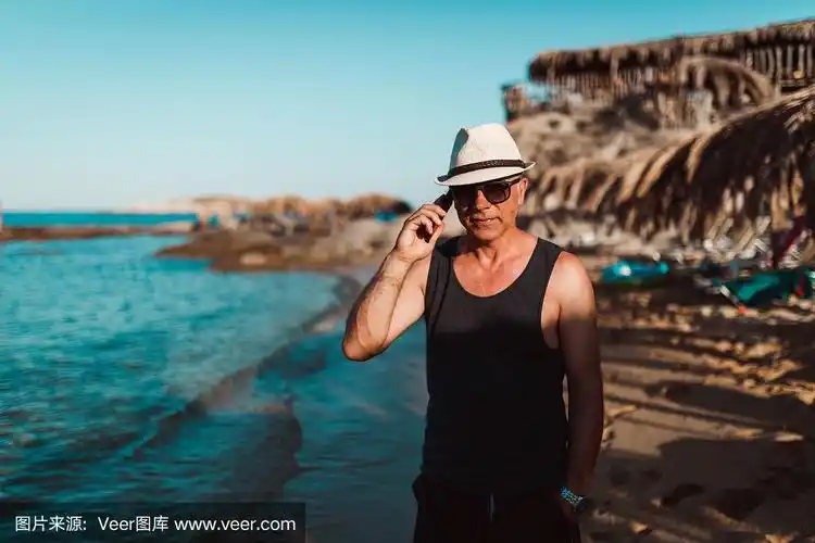 成熟的男人在海滩上用智能手机