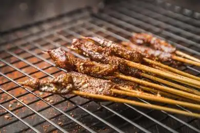 黑色烤架上放着几串撒着辣椒面的油炸牛肉小串